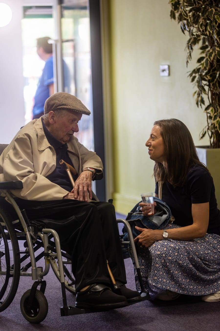 A woman kneeling to chat at eye level with an older man in a wheelchair at Hope Church